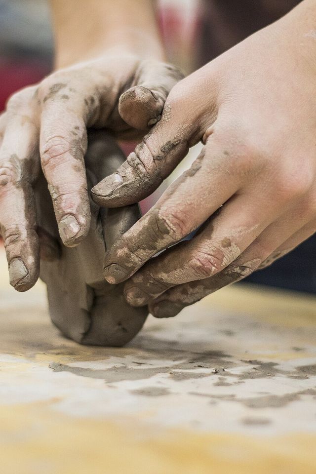 Two clay-covered hands wedging a lump of clay on a wooden table